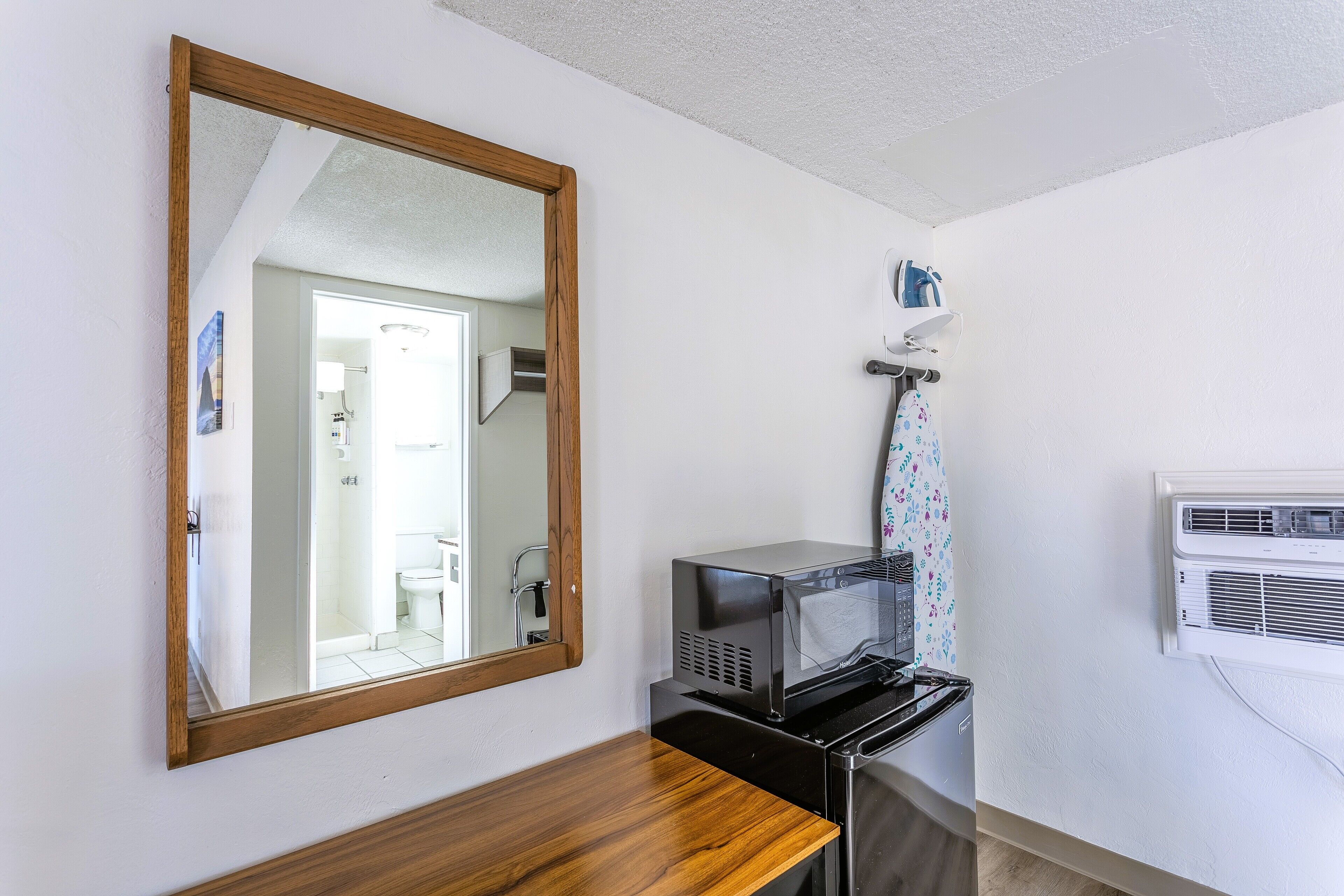 Une salle de bain avec un miroir encadré en bois, un four à micro-ondes et un appareil de climatisation fixé au mur.