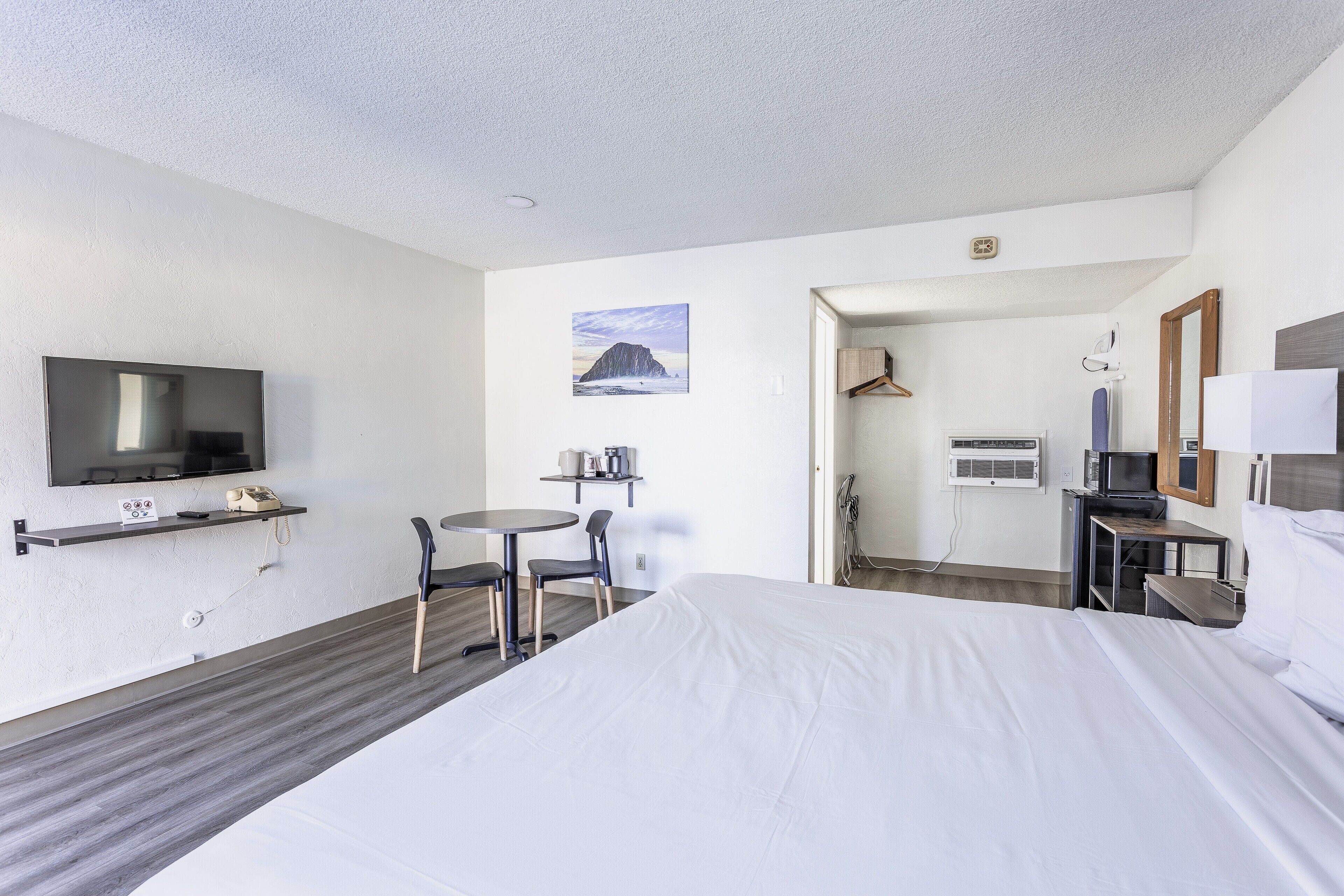 Habitación de hotel con una cama grande, televisor, escritorio con silla, una mesita y un cuadro en la pared.