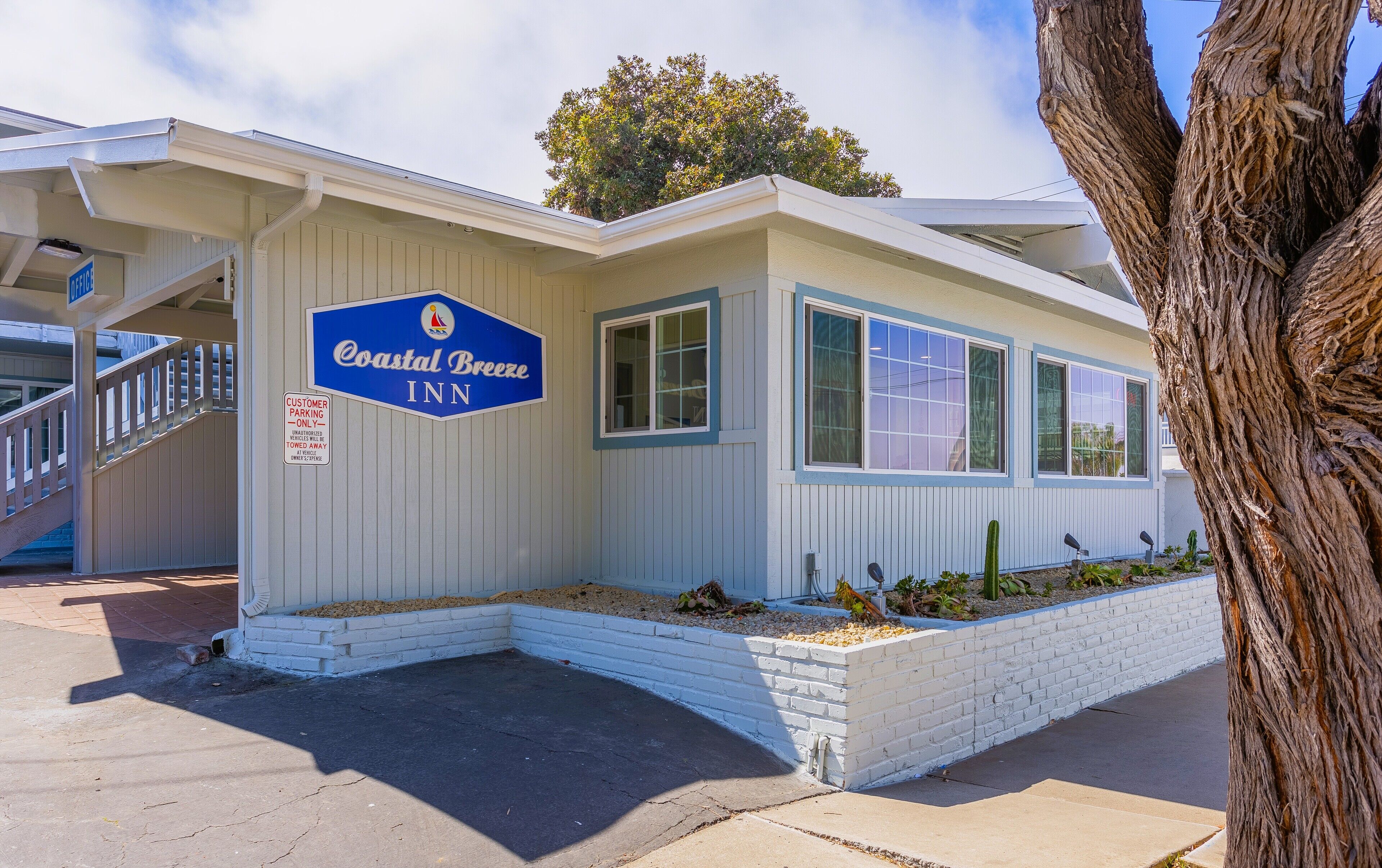 A Coastal Breeze Inn with a white exterior, a blue sign, and a small garden area.