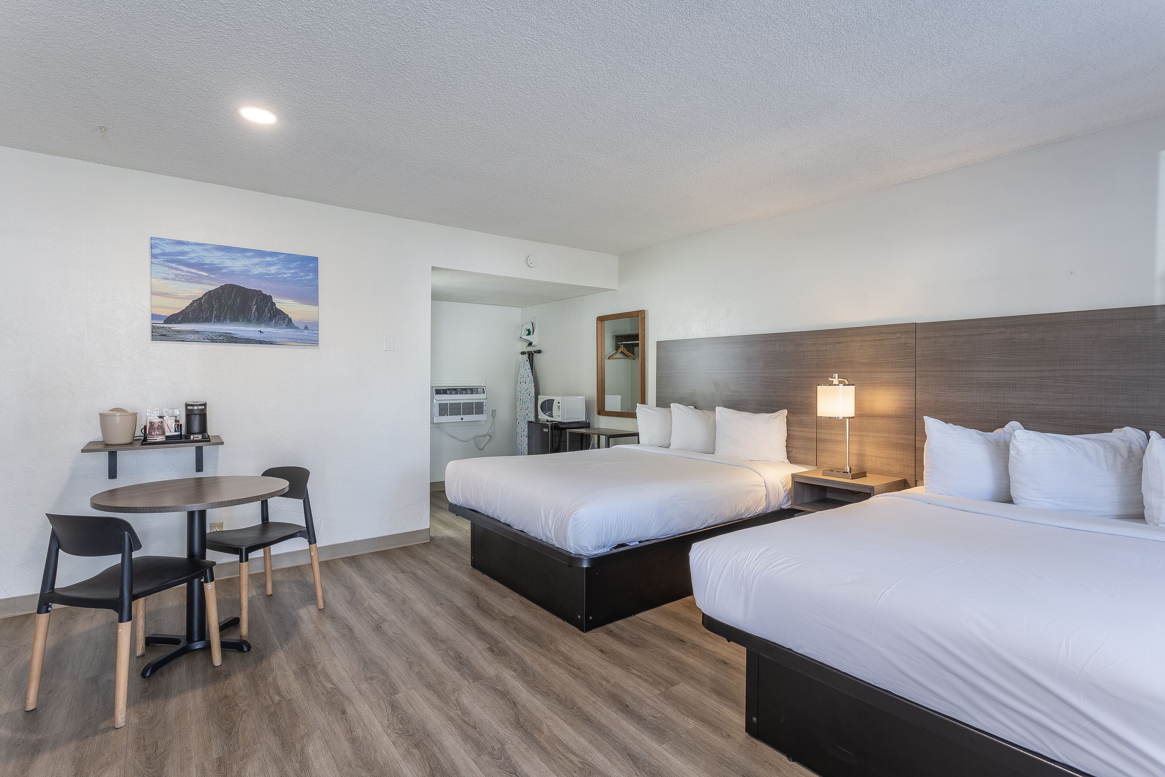 A hotel room with two beds, a dining table with chairs, a microwave, and a painting on the wall.