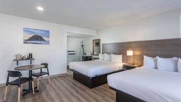 A hotel room with two beds, a dining table with chairs, a microwave, and a painting on the wall.