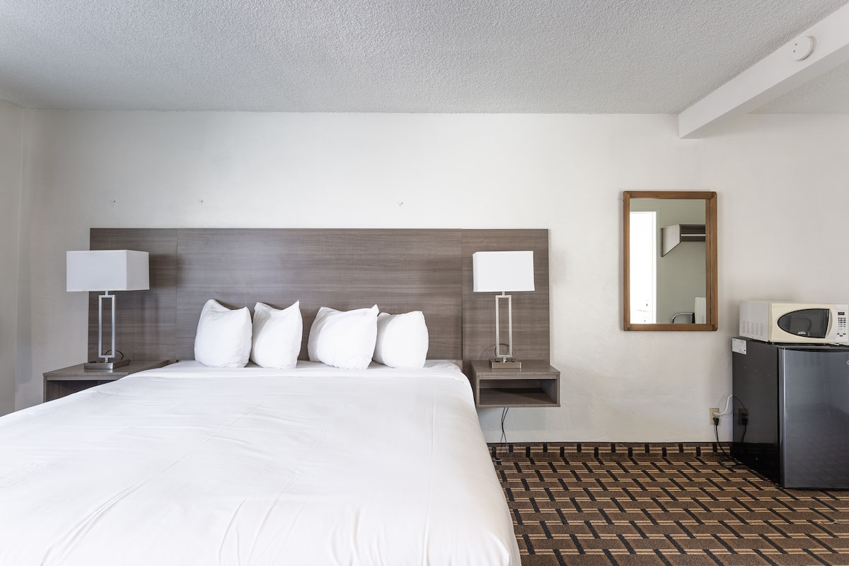 Una camera d'albergo con un letto grande, due comodini con lampade, un forno a microonde e uno specchio a parete.