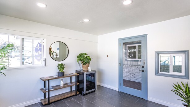 A modern entryway with a dark tiled floor, a wooden console table with a mirror, a potted plant, and a door leading to a brick exterior. - Coastal Breeze Inn (Morro Bay)