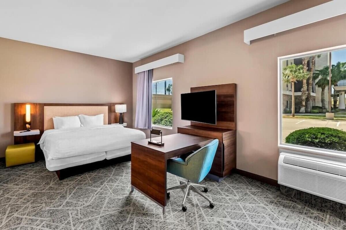 A hotel room with a bed, desk, chair, TV, and a large window with a view.