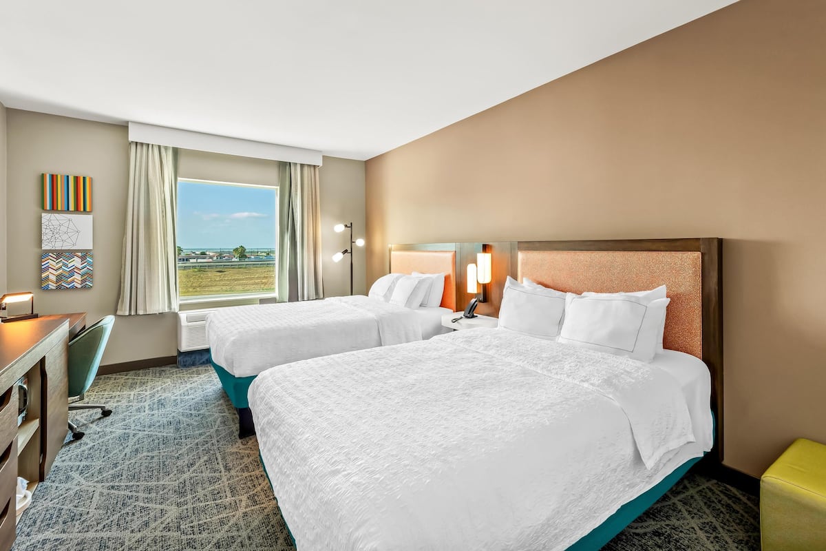 A hotel room with two beds, a desk, and a view of the outdoors.