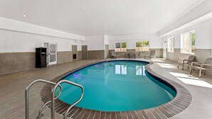 En inomhuspool med en böjd design, omgiven av ett kaklat golv och kaklade väggar, och utrustad med en metallstege.