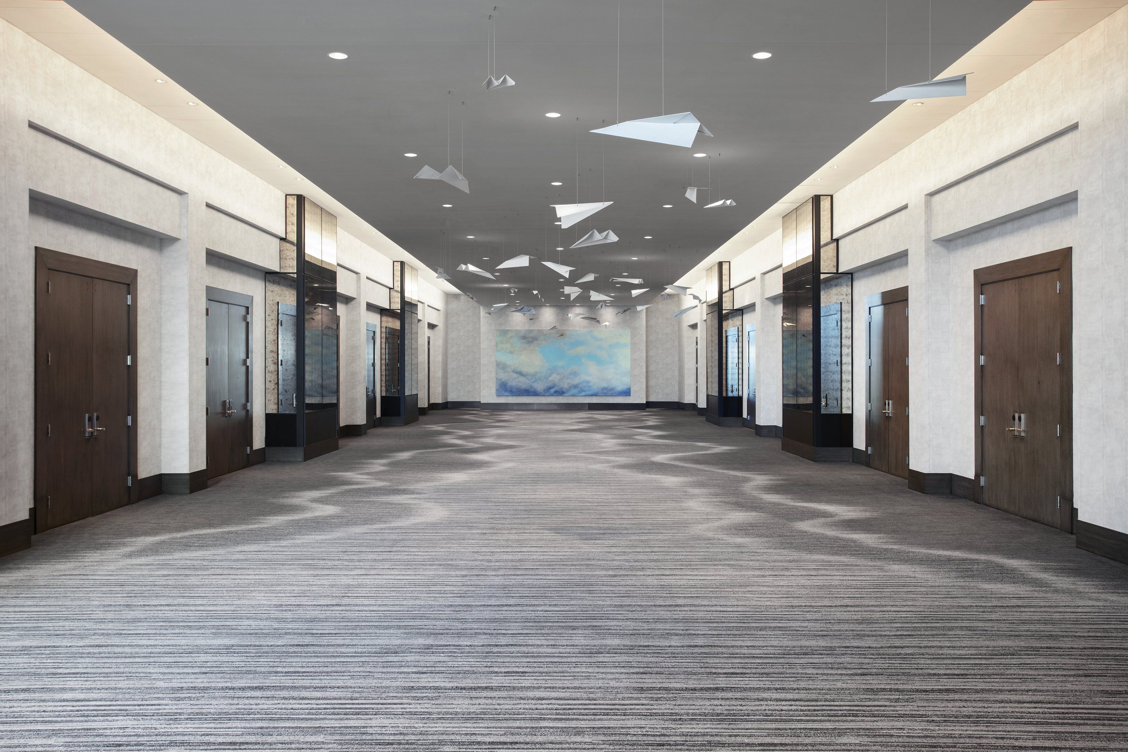 A spacious hotel lobby with a carpeted floor, multiple doors, and hanging pendant lights.