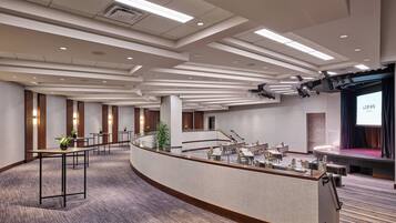 A modern hotel lobby with a curved reception desk, multiple seating areas, and a stage for presentations.