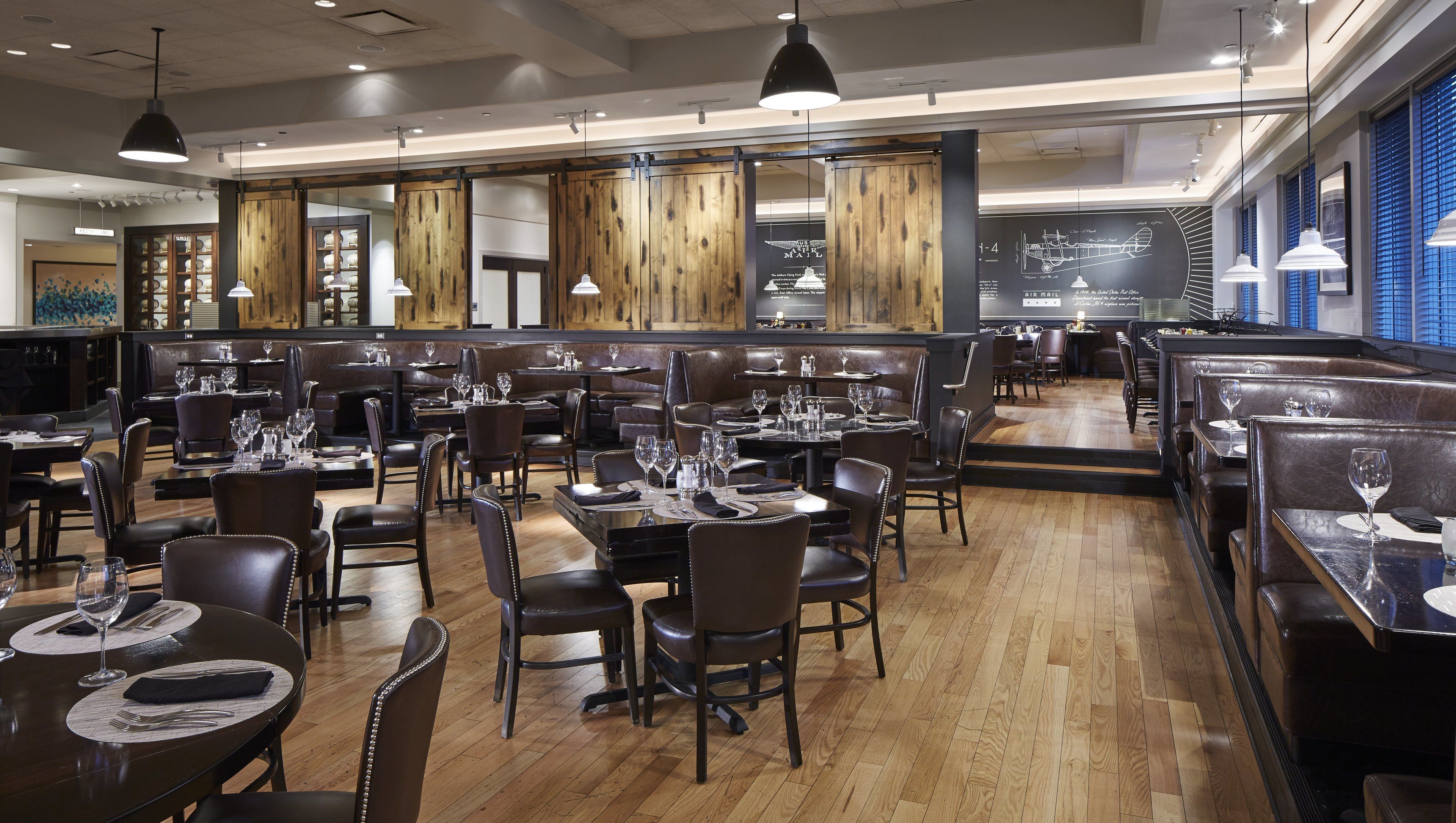 A restaurant with multiple dining areas, wooden floors, and pendant lighting.