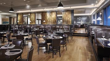 A restaurant with multiple dining areas, wooden floors, and pendant lighting.
