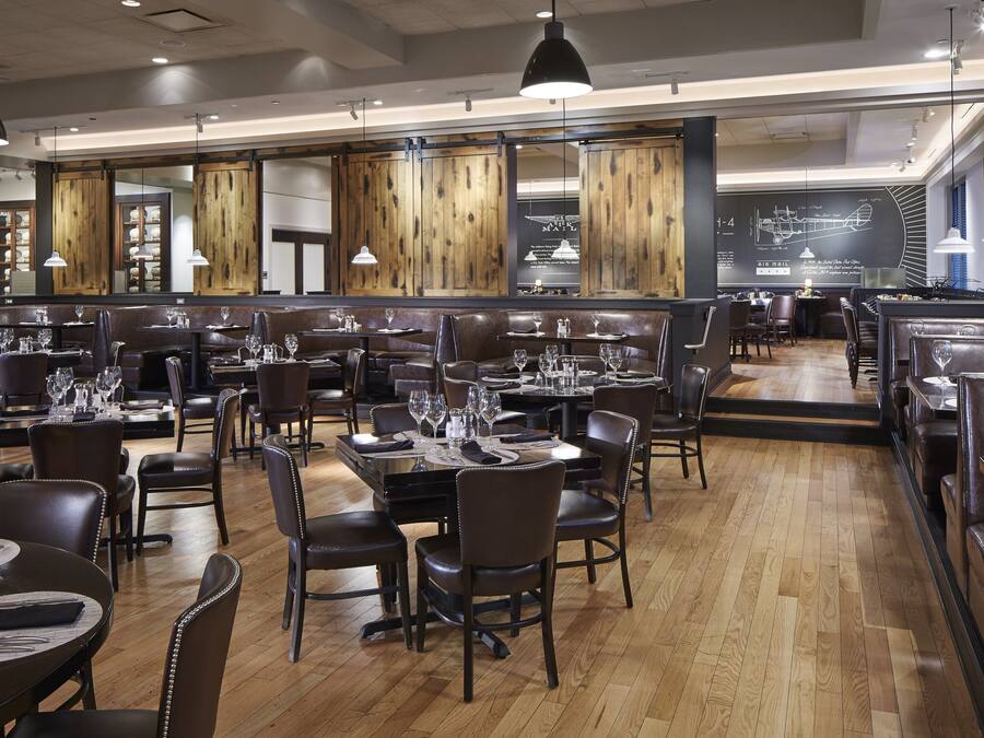 A restaurant with multiple dining areas, wooden floors, and pendant lighting.