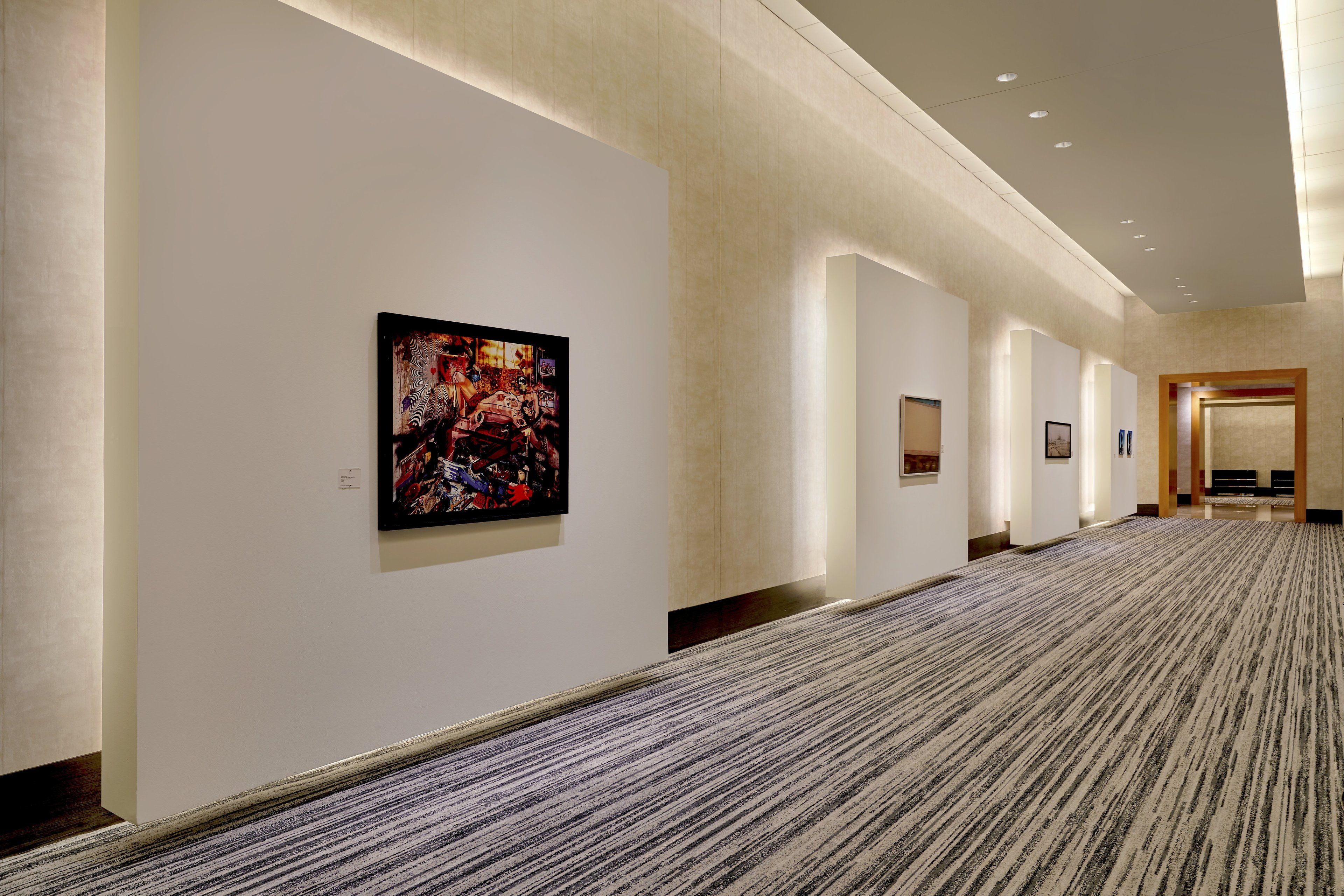 A hallway with a patterned carpet, white walls, and framed artwork.