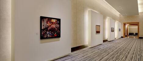 A hallway with a patterned carpet, white walls, and framed artwork.