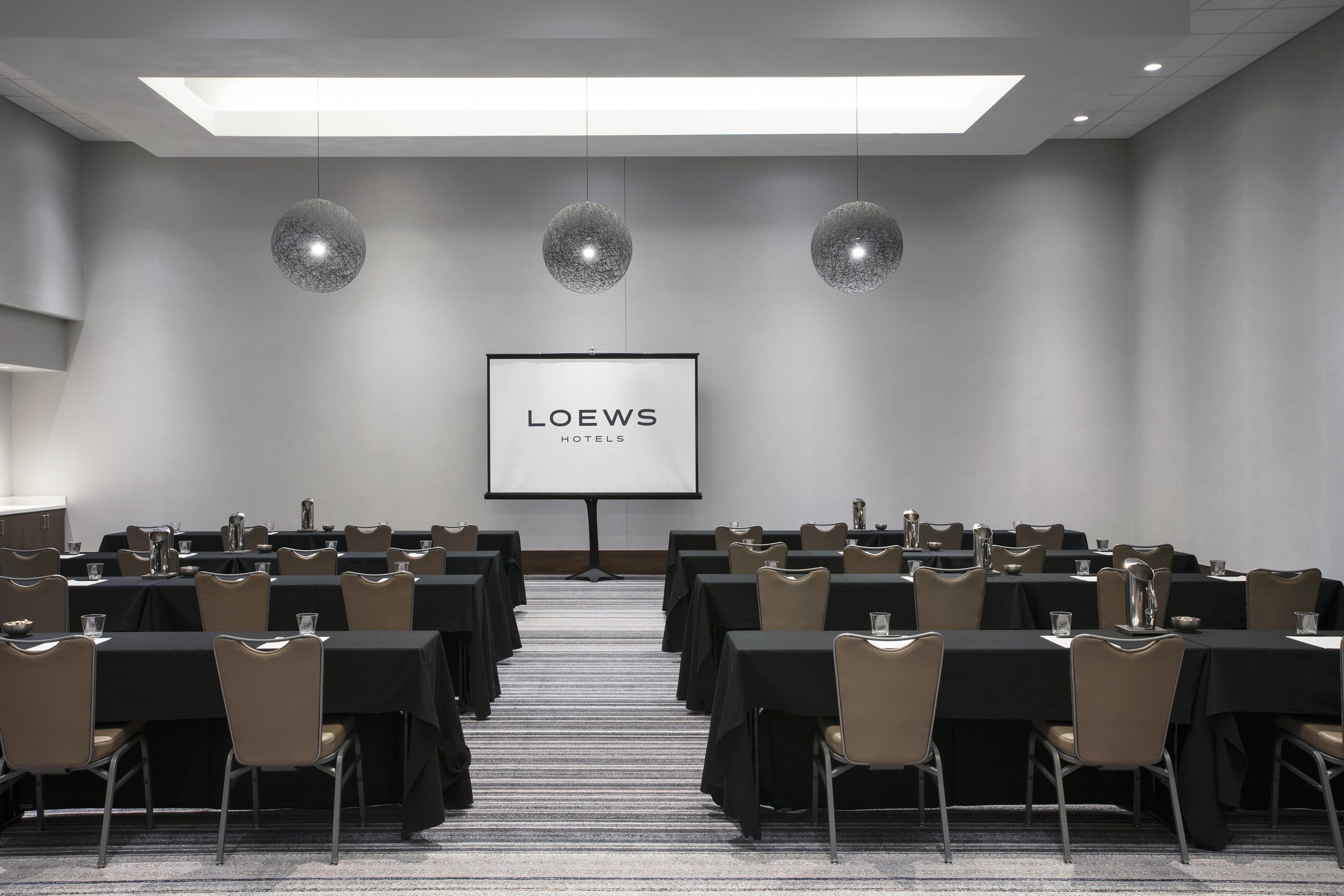 Un salón de conferencias con mesas y sillas, una pantalla de proyector y un logotipo en la pared.