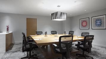 A conference room with a long table, six chairs, a modern pendant light, and two framed artworks on the wall.