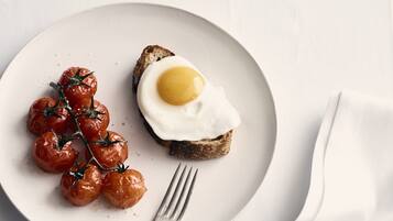 A plate with a fried egg on toast and cherry tomatoes, a fork, and a cup of coffee on a white table.