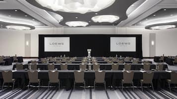 Une salle de conférence dotée de plusieurs tables et chaises, d’un grand écran affichant le nom « LOEWS HOTELS », et d’un design de plafond moderne.
