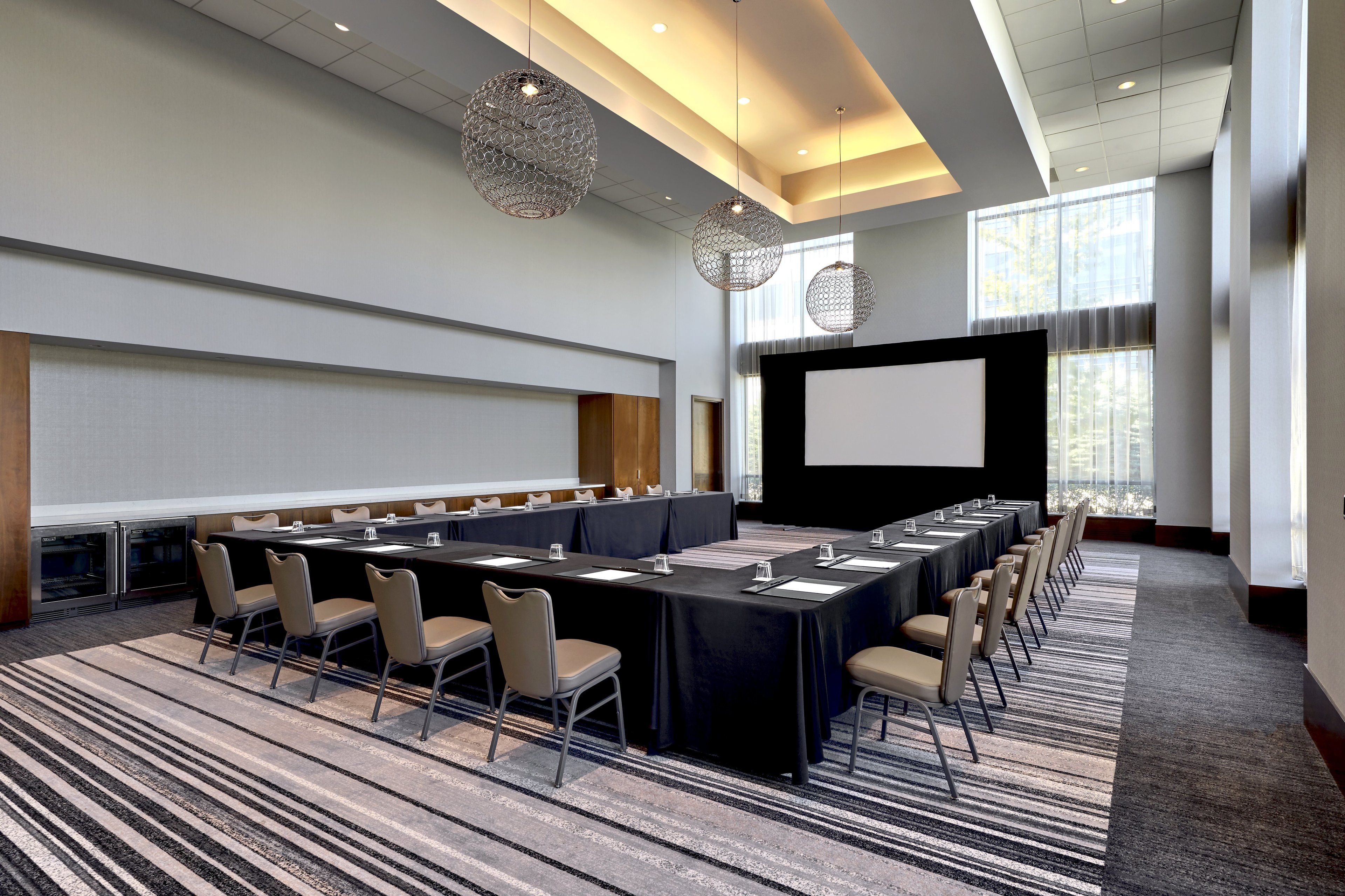 A conference room with a long table, chairs, a projector screen, and hanging pendant lights.