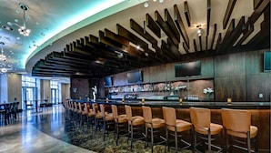 A modern bar area with a curved ceiling, wooden slats, and a bar counter with stools.