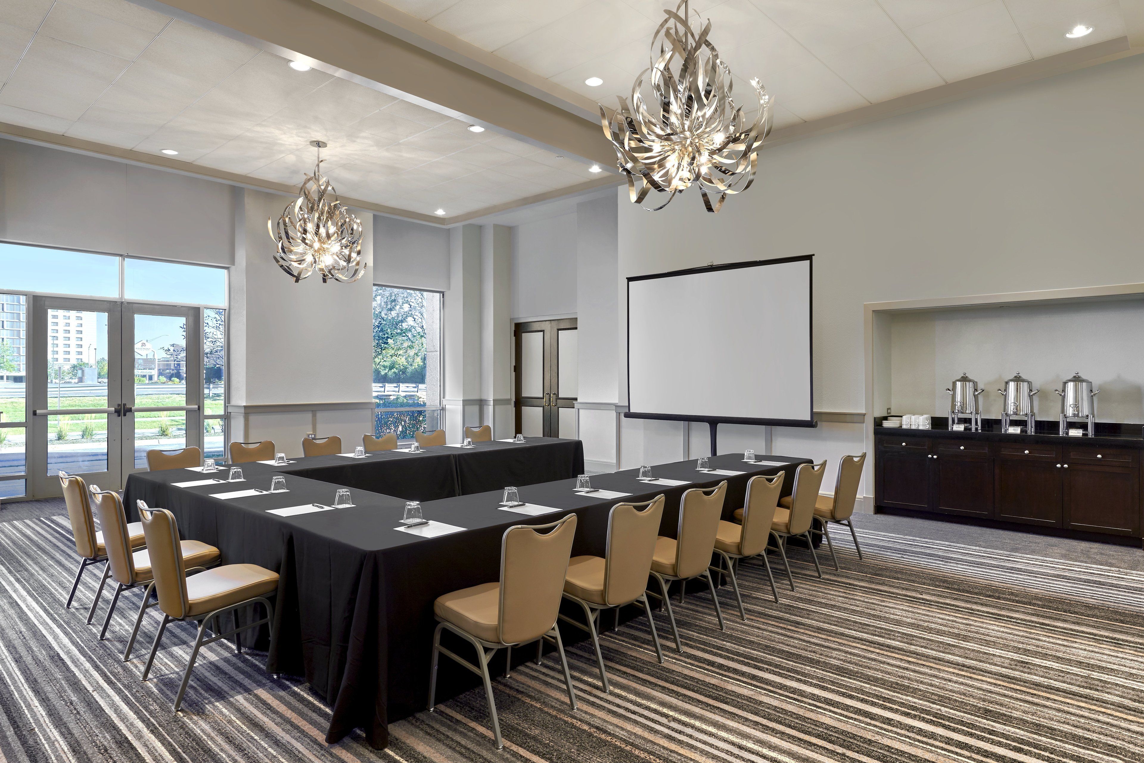 A conference room with a long table, chairs, a projector screen, and a buffet area.