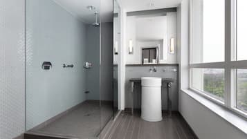 Un baño moderno con cabina de ducha de vidrio, un lavamanos y ventana con vistas a la ciudad.
