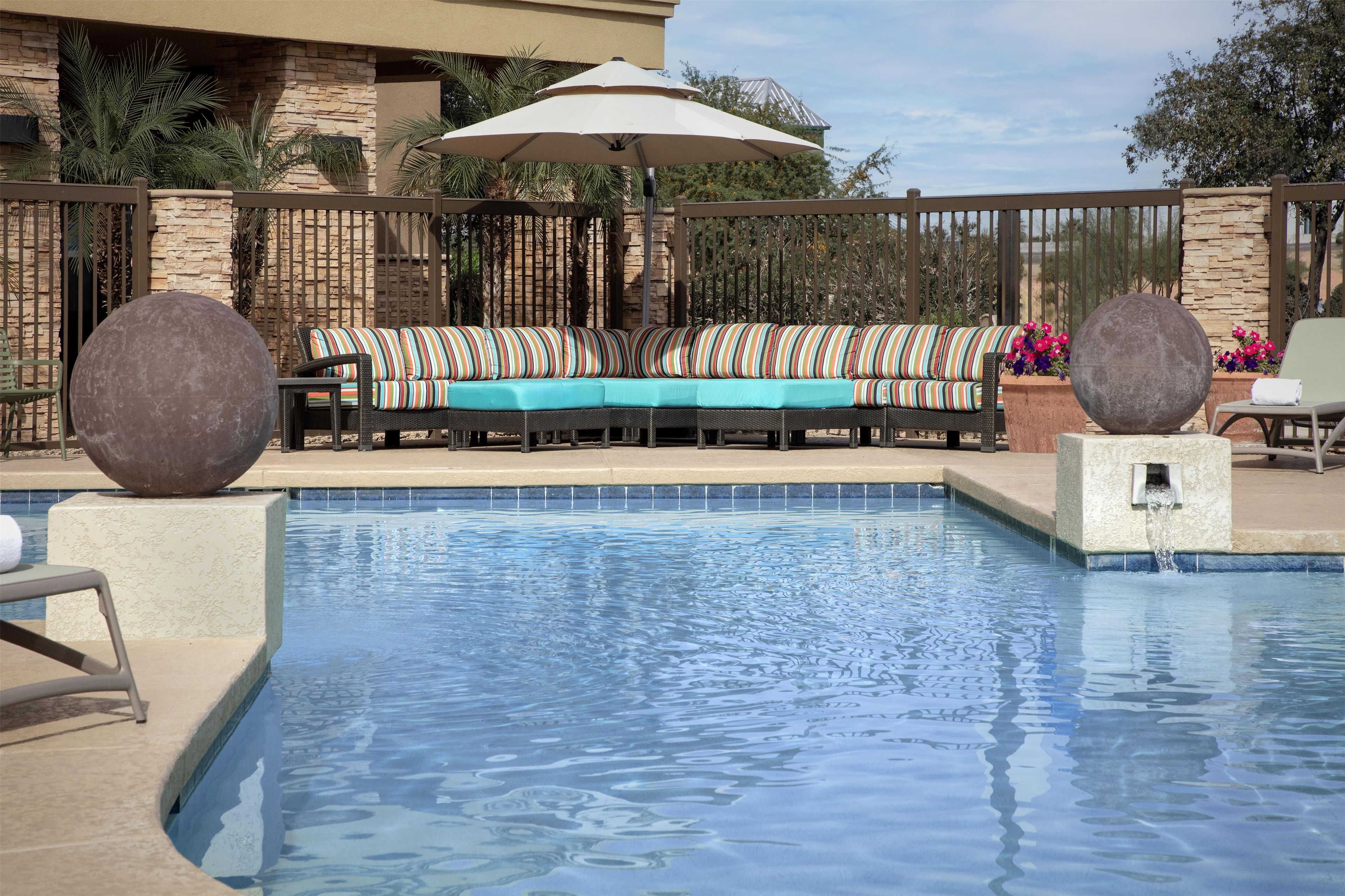 A pool area with a seating arrangement, a stone wall, and a fence.