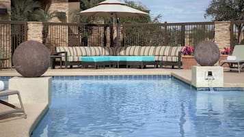 A pool area with a seating arrangement, a stone wall, and a fence.