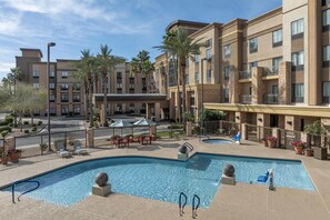 Un hotel con piscina, zona de estar exterior y palmeras.