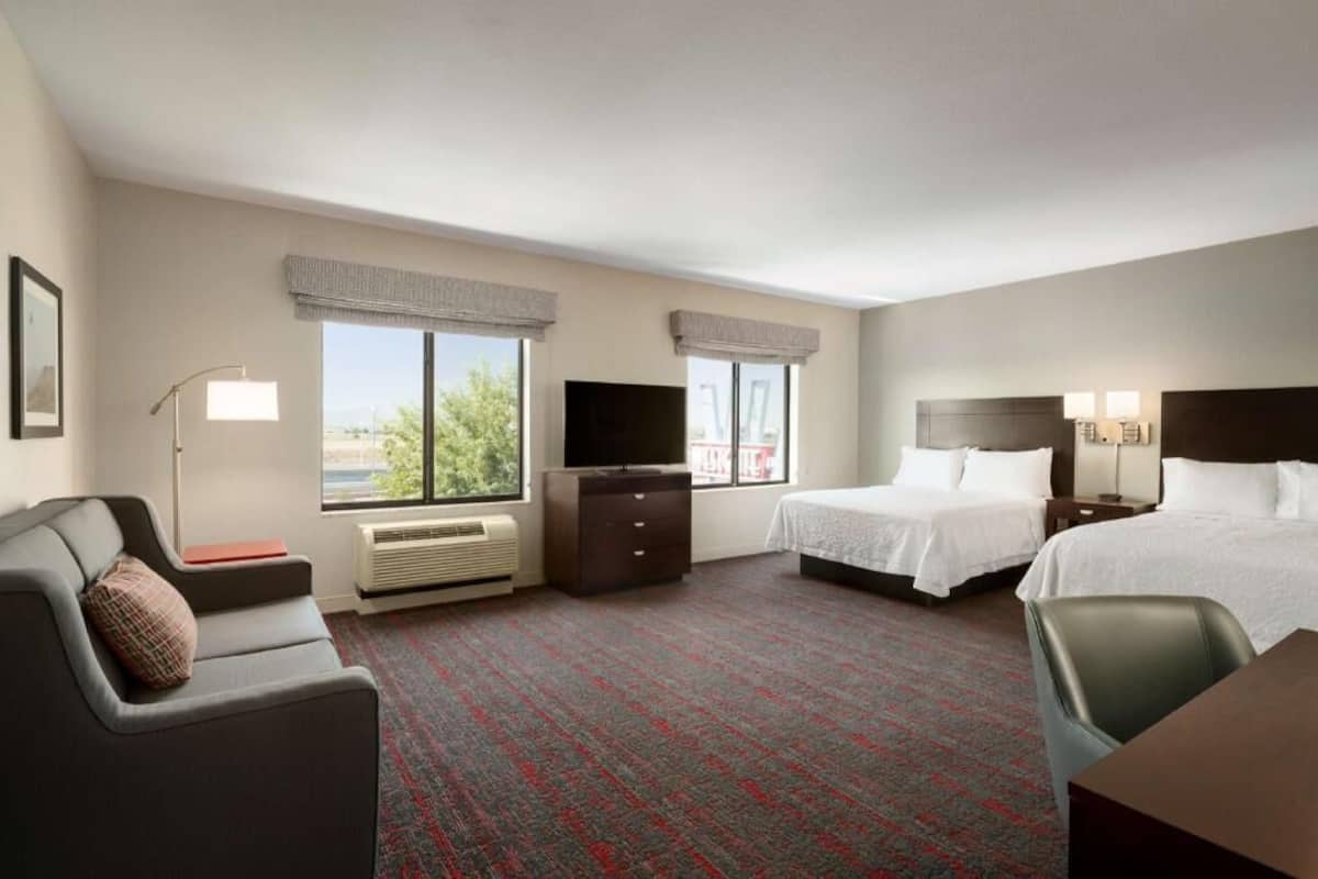 Ein Hotelzimmer mit zwei Betten, einem Schreibtisch, einem Stuhl, einem Fernseher und einem Fenster mit Blick.