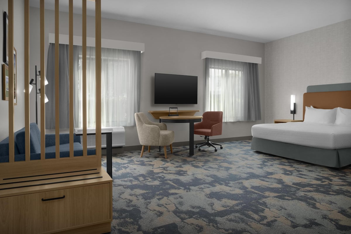 Ein Hotelzimmer mit Bett, Schreibtisch, zwei Stühlen, einem Fernseher und einem Holzschrank.