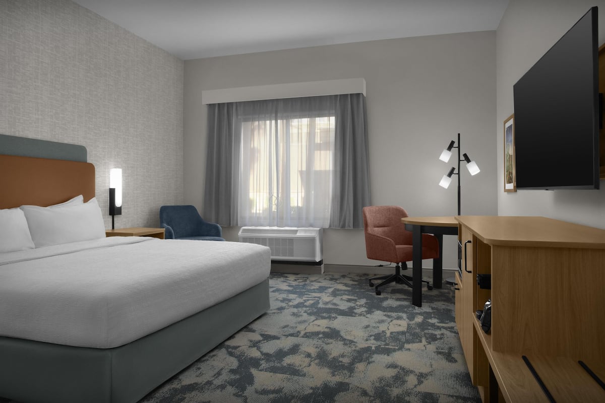 Ein Hotelzimmer mit einem großen Bett, einem Schreibtisch, einem Sessel, einer Klimaanlage und einem Fernseher an der Wand.