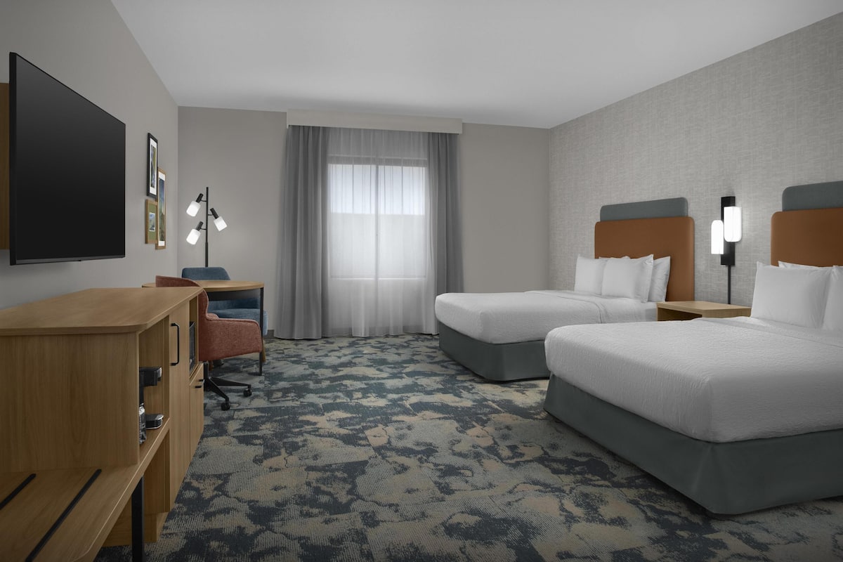 Ein Hotelzimmer mit zwei Betten, einem Schreibtisch, einem Sessel, einem Fernseher und einem Fenster mit Vorhängen.