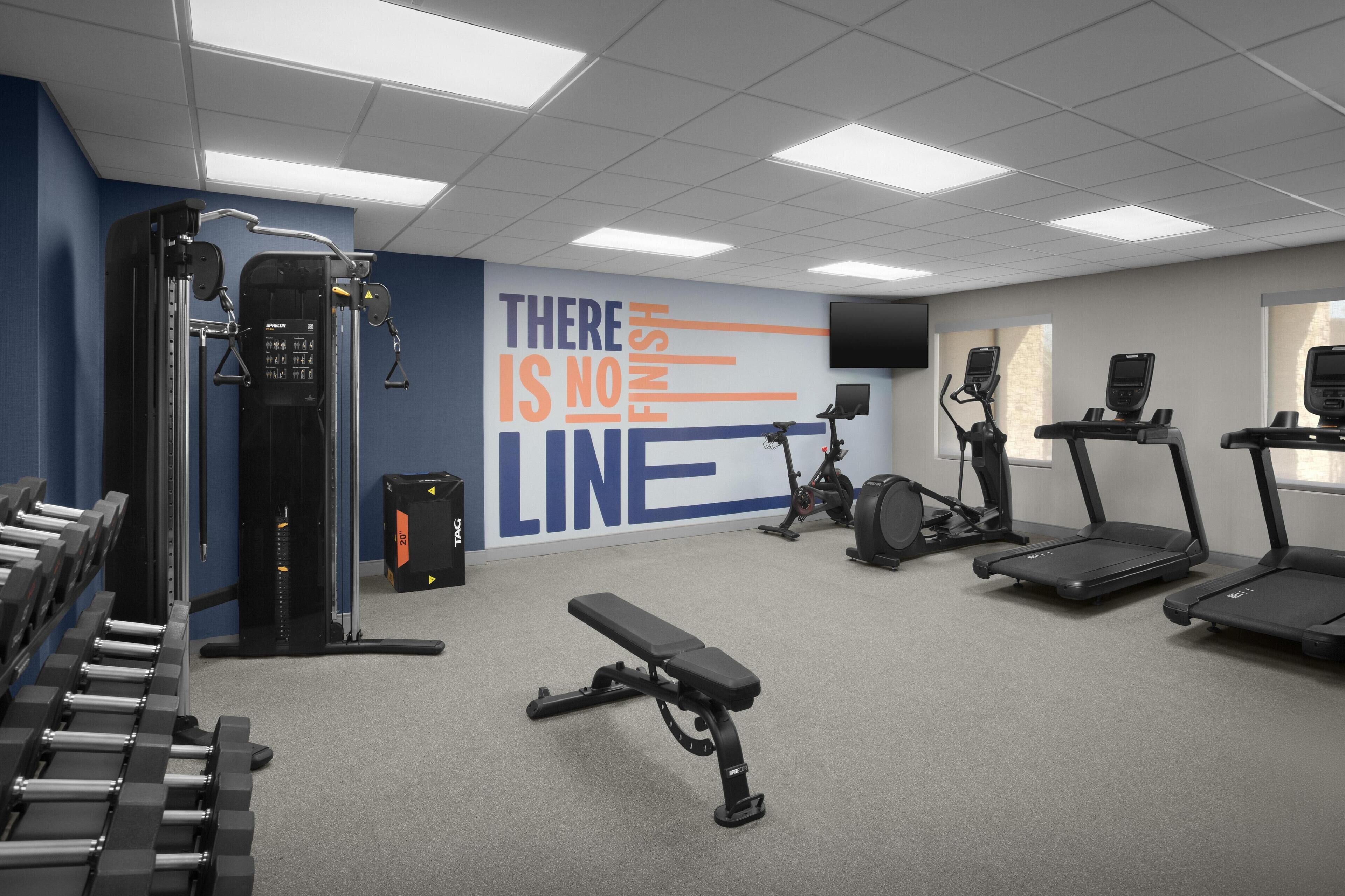 A gym with exercise equipment, a bench, treadmills, and a motivational wall.