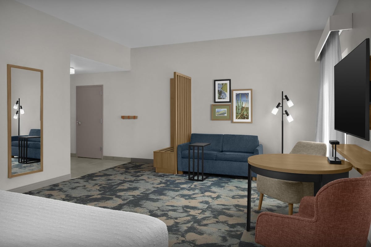 Ein Hotelzimmer mit einem Bett, einem Schlafsofa, einem kleinen Tisch, einem Fernseher und einem Spiegel.
