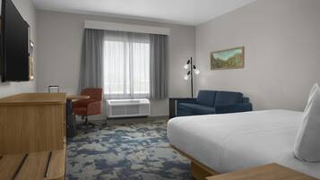 A hotel room with a bed, a desk, a chair, a standing lamp, and a window with curtains.