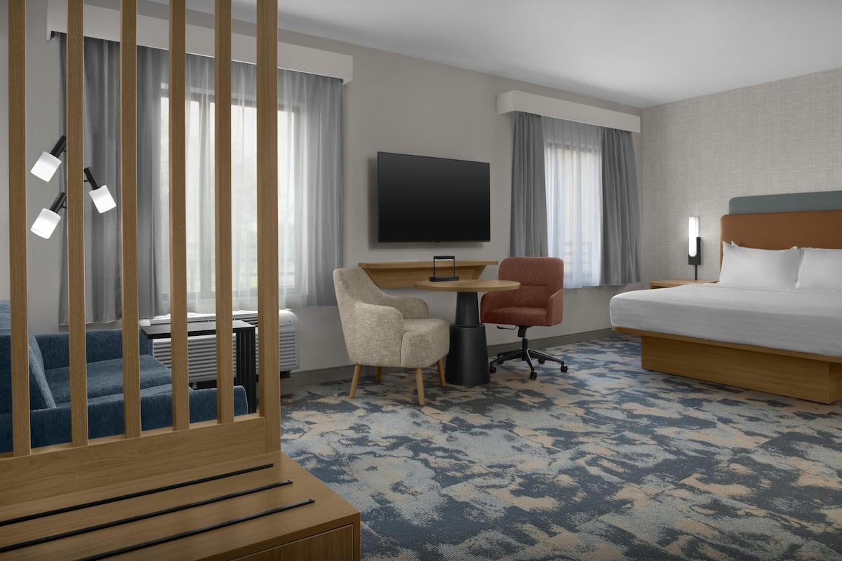 Ein Hotelzimmer mit einem Bett, einem Schreibtisch mit Stuhl, einem Fernseher und einem großen Fenster mit Vorhängen.