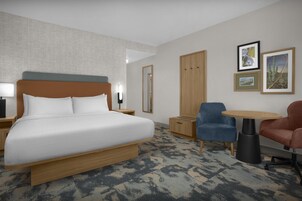 Habitación de hotel con una cama grande, un escritorio, una silla, una mesita y cuadros en la pared.