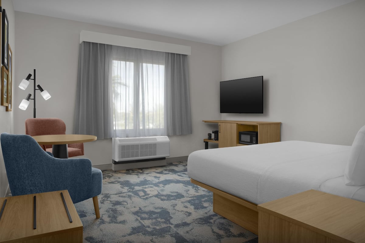 Ein Hotelzimmer mit Bett, Schreibtisch, Stuhl, Fernseher und einem Fenster mit Vorhängen.