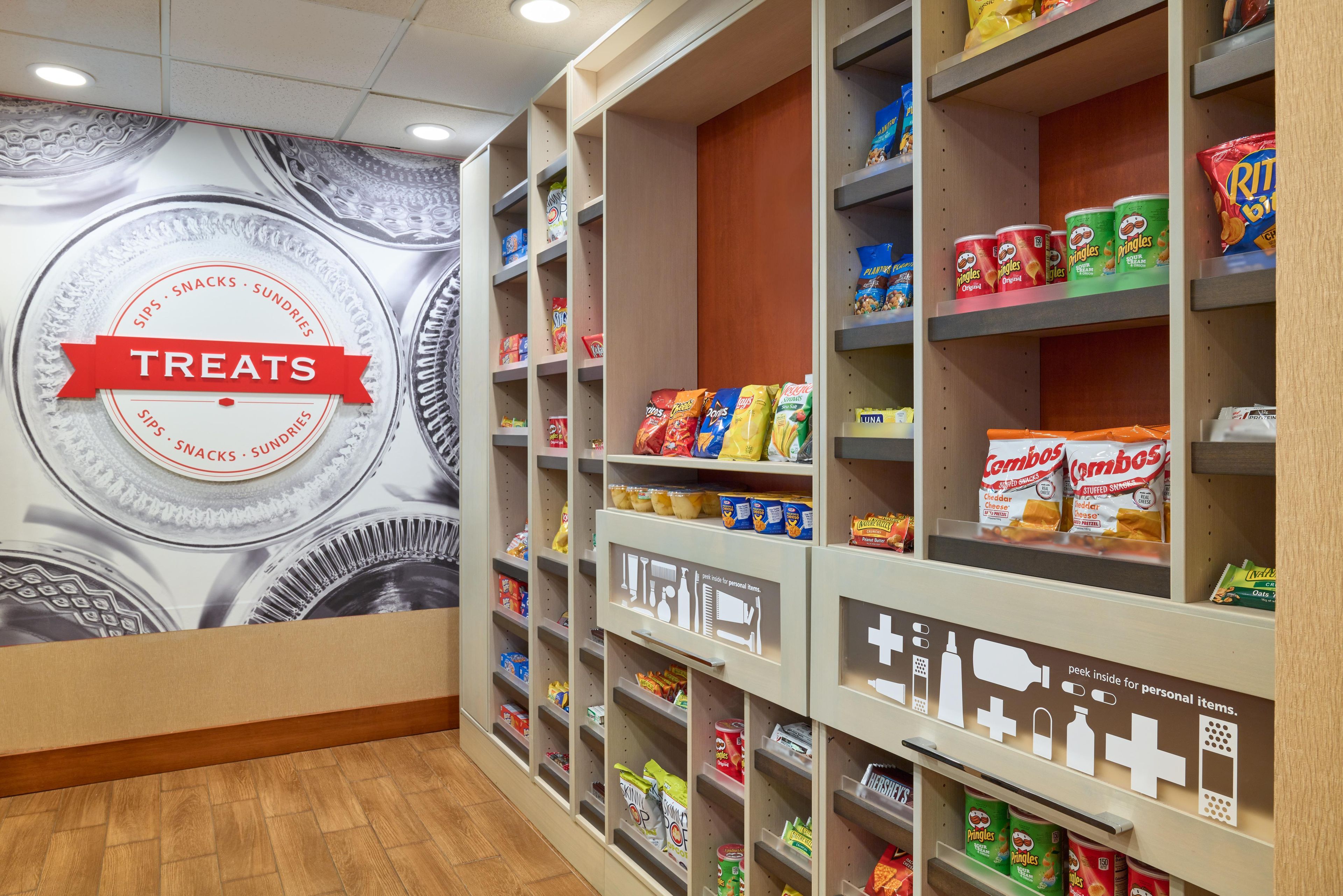 A snack aisle with shelves stocked with various snacks and a wall with a 'TREATS' sign.
