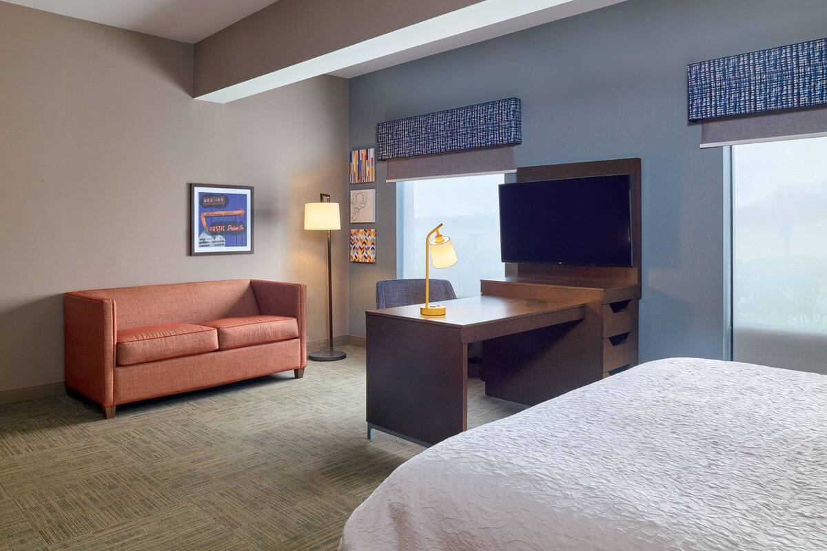 Quarto de hotel com sofá, escrivaninha, televisão e cama.