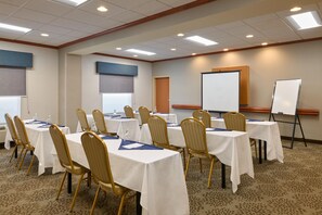 Une salle de conférence équipée de tables, de chaises, d’un tableau blanc et d’un écran de projection.