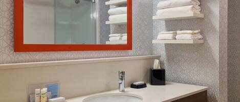 A bathroom with a large mirror, a sink, and shelves with folded towels.