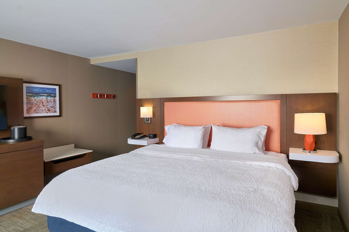 Quarto de hotel com uma cama grande, uma mesa com telefone, uma luminária e um quadro na parede.
