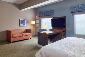 A hotel room with a bed, a desk, a sofa, a TV, and artwork on the wall. - Hampton Inn & Suites Providence/Smithfield (Smithfield)