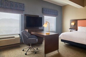 A hotel room with a bed, a desk with a chair, a television, a lamp, and a window with a view.