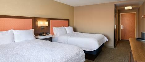 A hotel room with two beds, a nightstand, a lamp, and a door leading to another room.