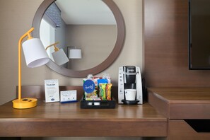 A hotel desk with a lamp, a coffee maker, a tray of snacks, a welcome card, and a premium internet access sign.