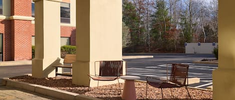 An outdoor seating area with two chairs and a table, surrounded by a low brick wall and a gravel path.