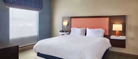 A hotel room with a large bed, two bedside tables with lamps, a nightstand, and a window with a view of a car.