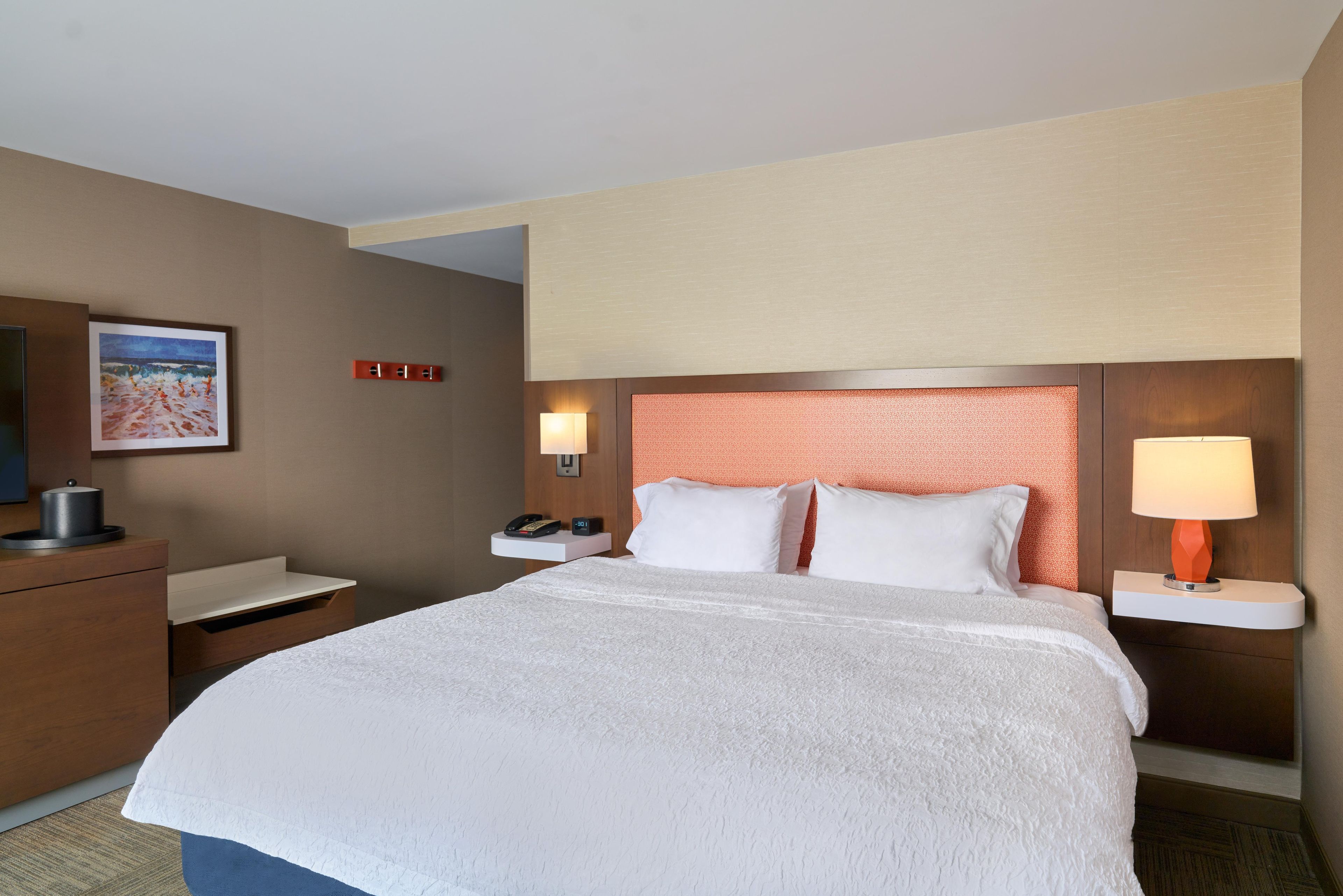 A hotel room with a large bed, a desk with a lamp, a phone, and a painting on the wall.